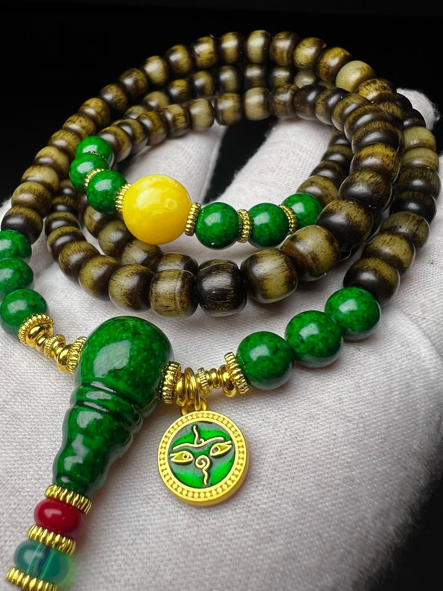 108-bead dark mala with a green gourd pendant resting on a white cotton glove