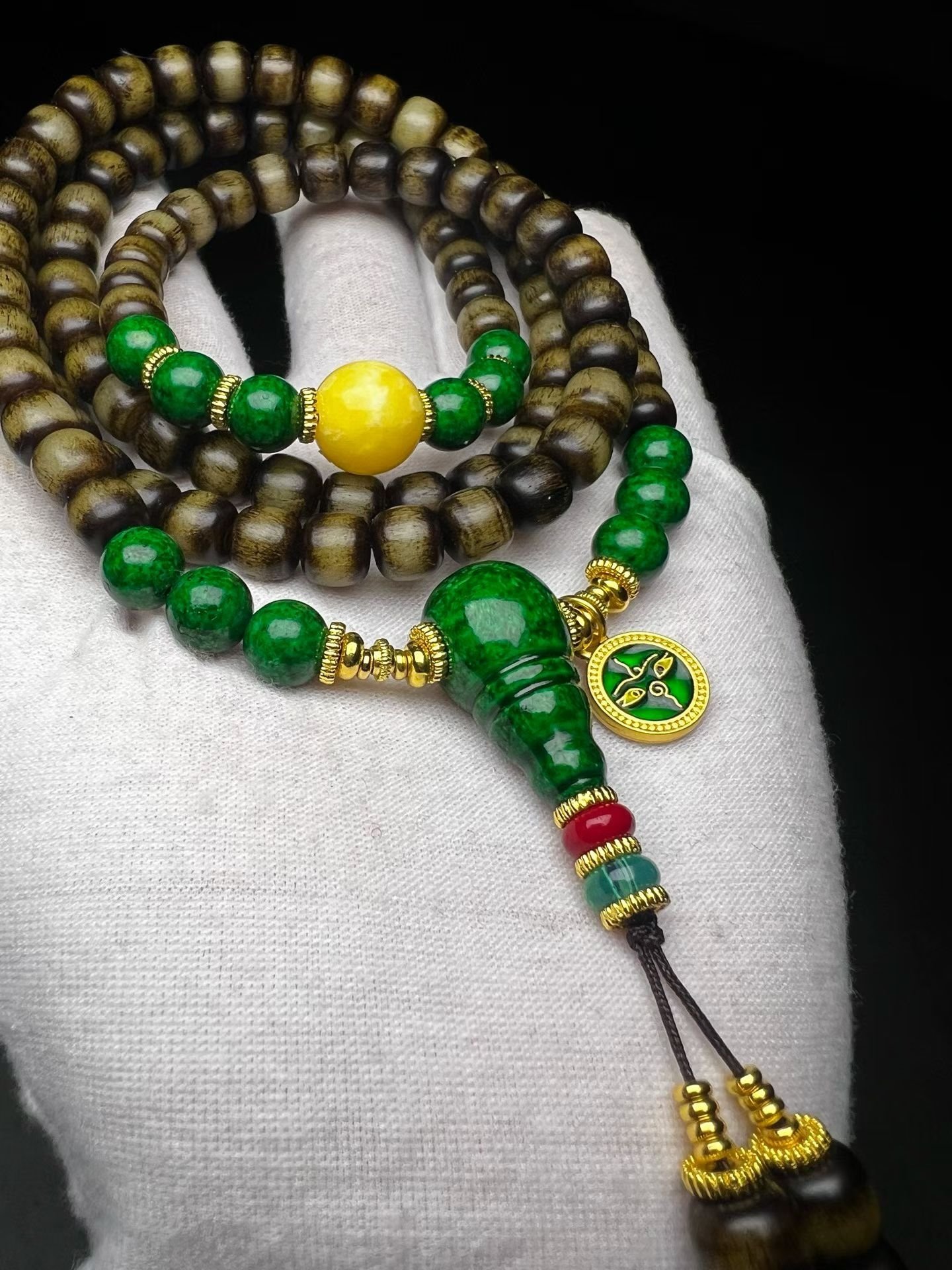 108-bead dark mala with a green gourd pendant resting on a white cotton glove