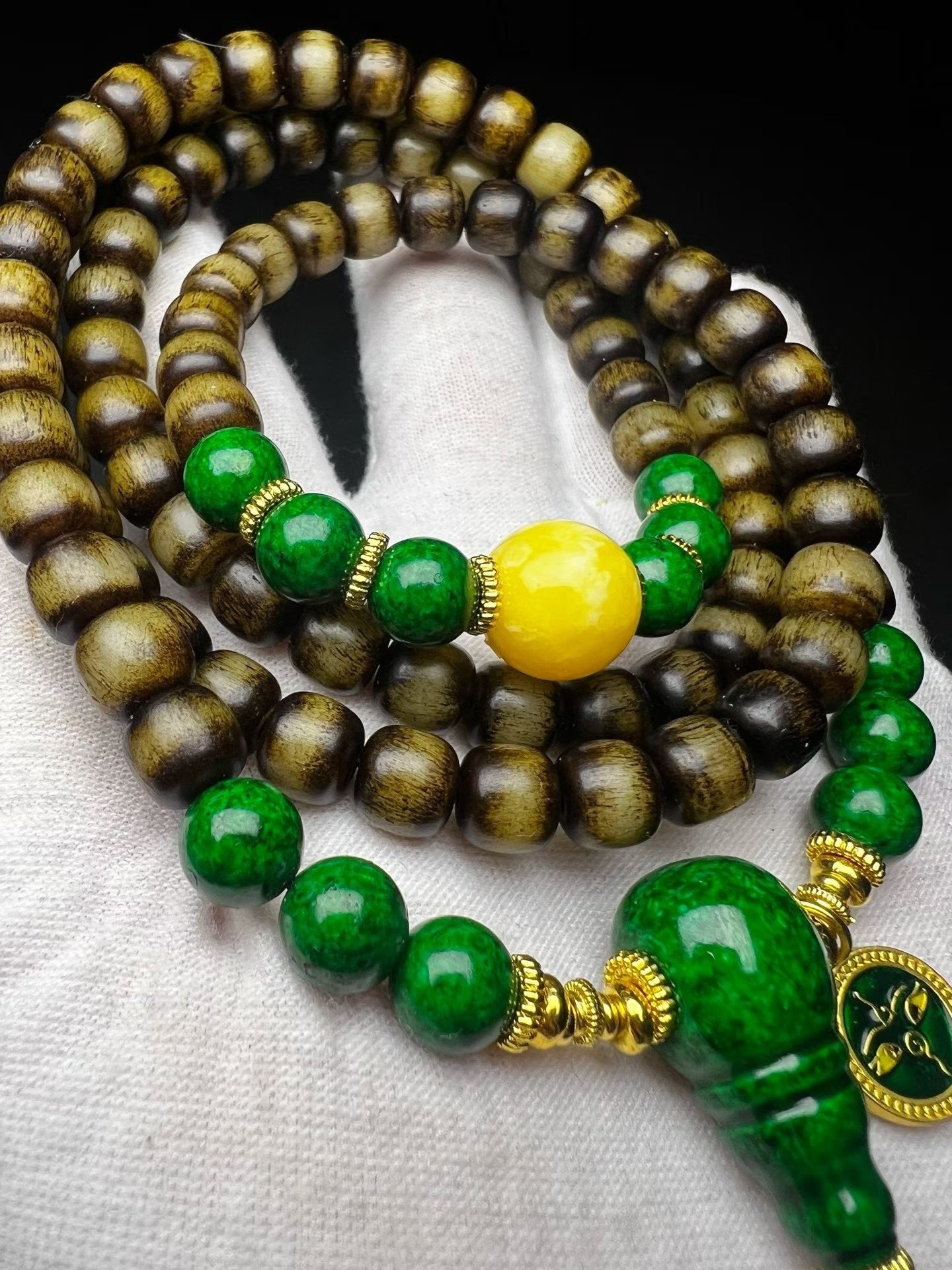 108-bead dark mala with a green gourd pendant resting on a white cotton glove