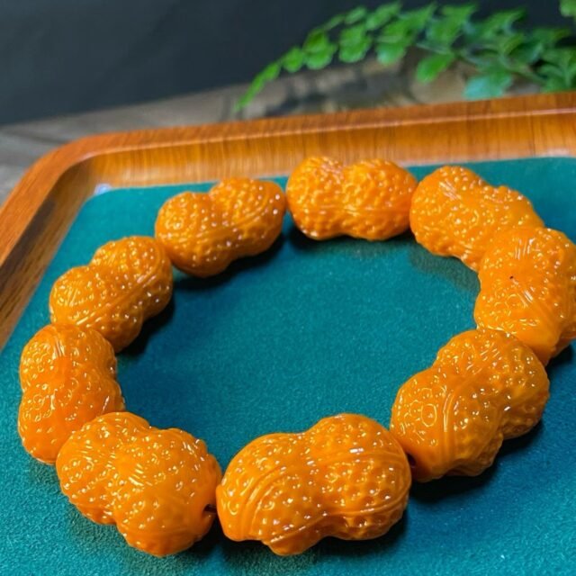 Bracelet of orange peanut-shaped carved beads with red dots, in a bamboo box