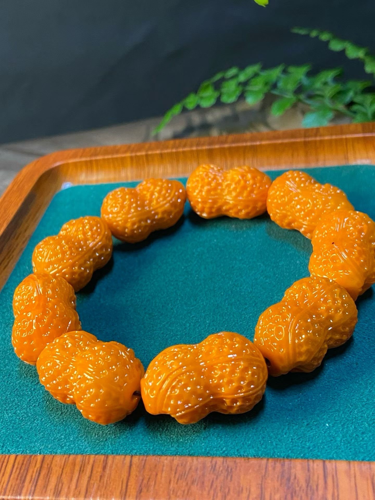 Bracelet of orange peanut-shaped carved beads with red dots, in a bamboo box