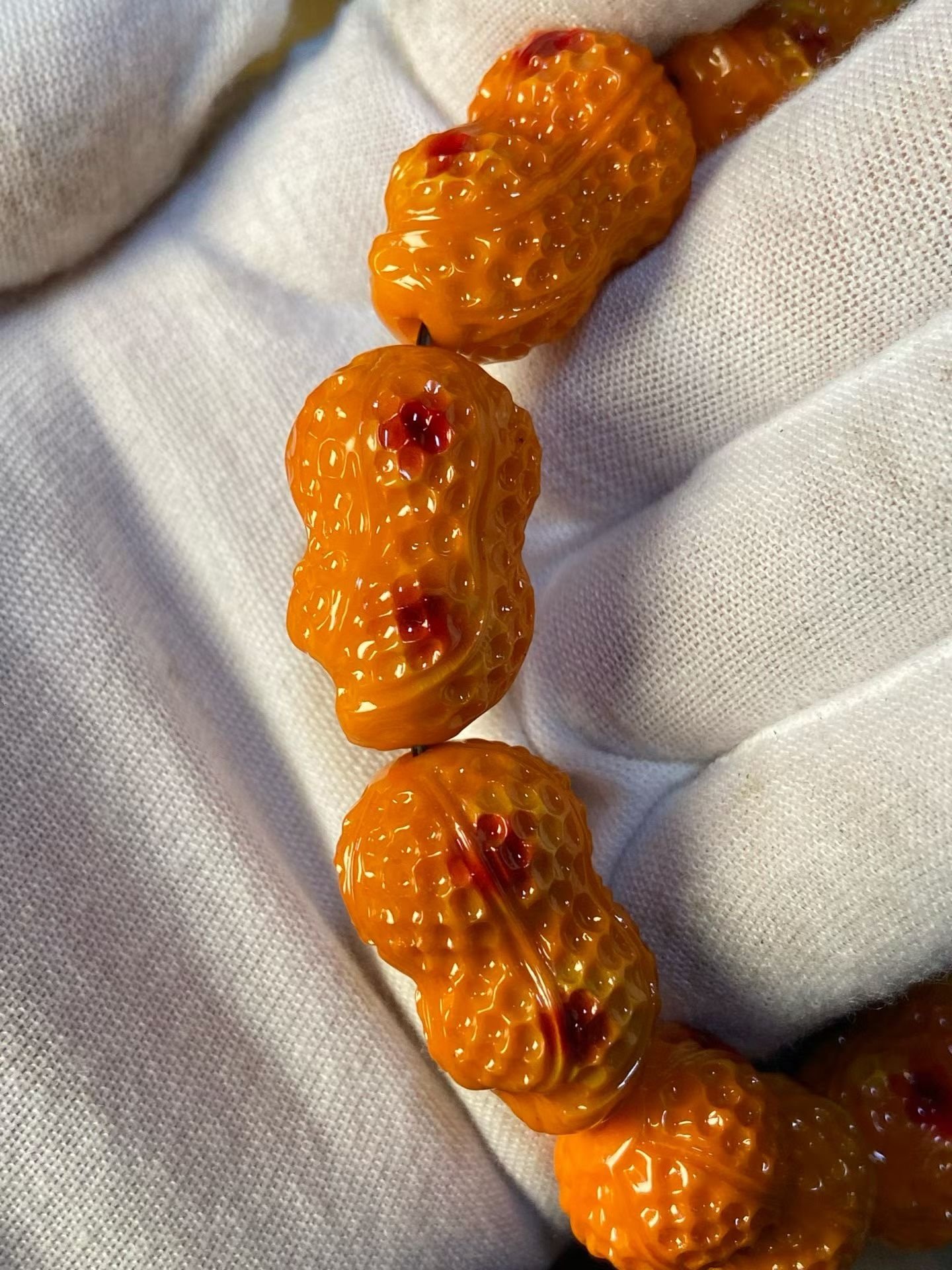 Bracelet of orange peanut-shaped carved beads with red dots, in a bamboo box
