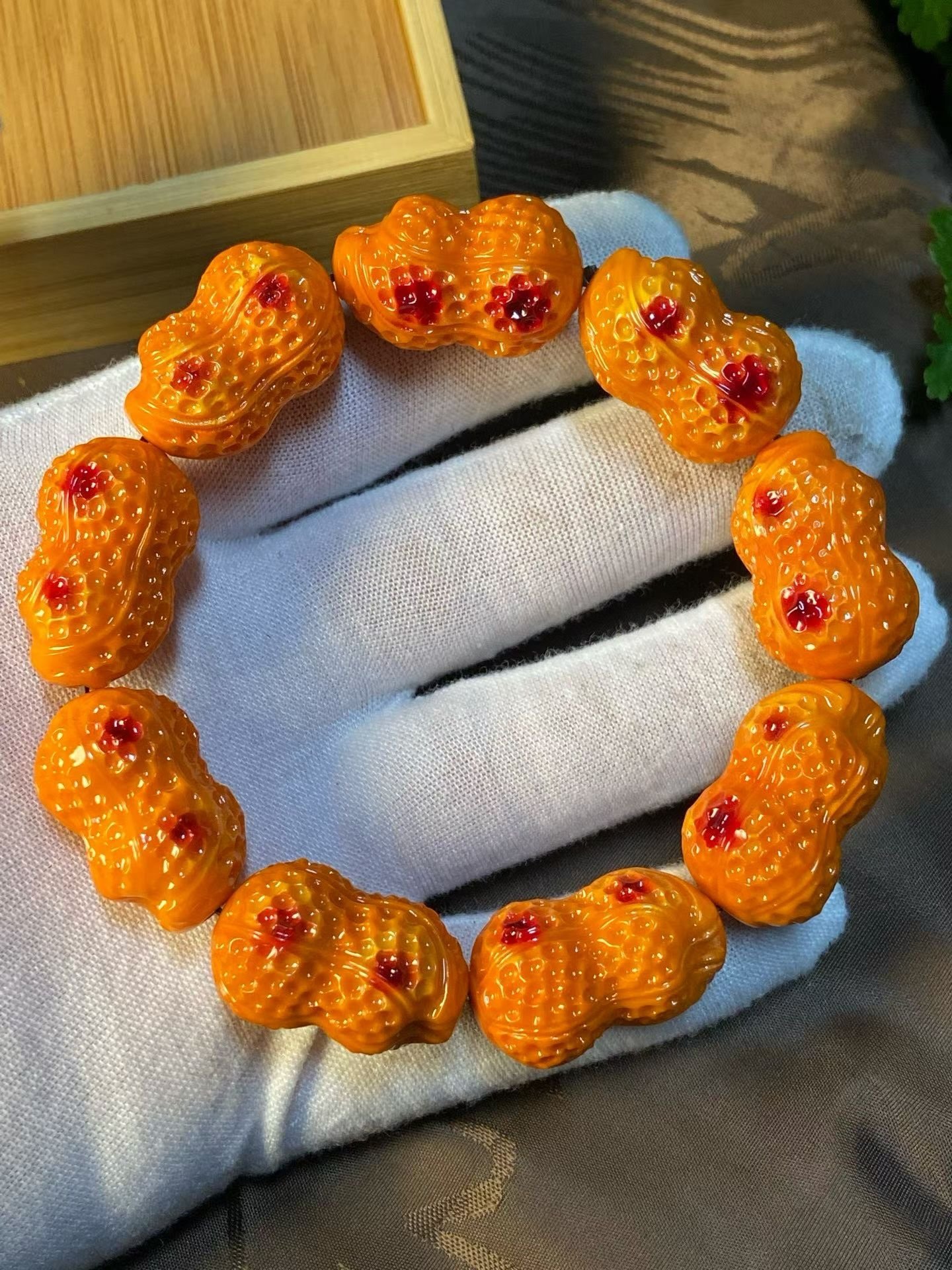 Bracelet of orange peanut-shaped carved beads with red dots, in a bamboo box