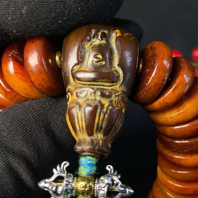 Stacked amber disc beads with a carved buddha head and a silvered vajra pendant