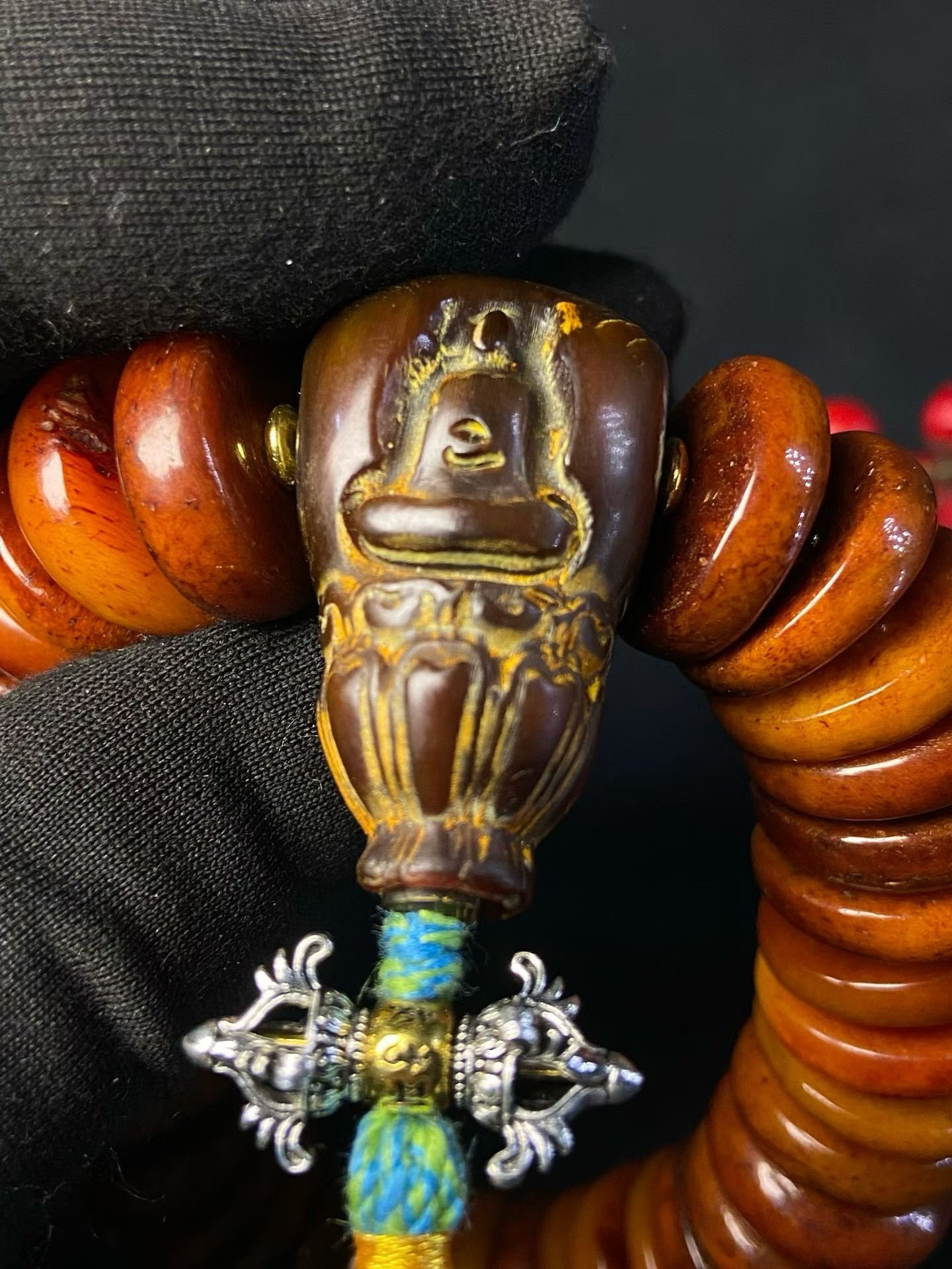 Stacked amber disc beads with a carved buddha head and a silvered vajra pendant