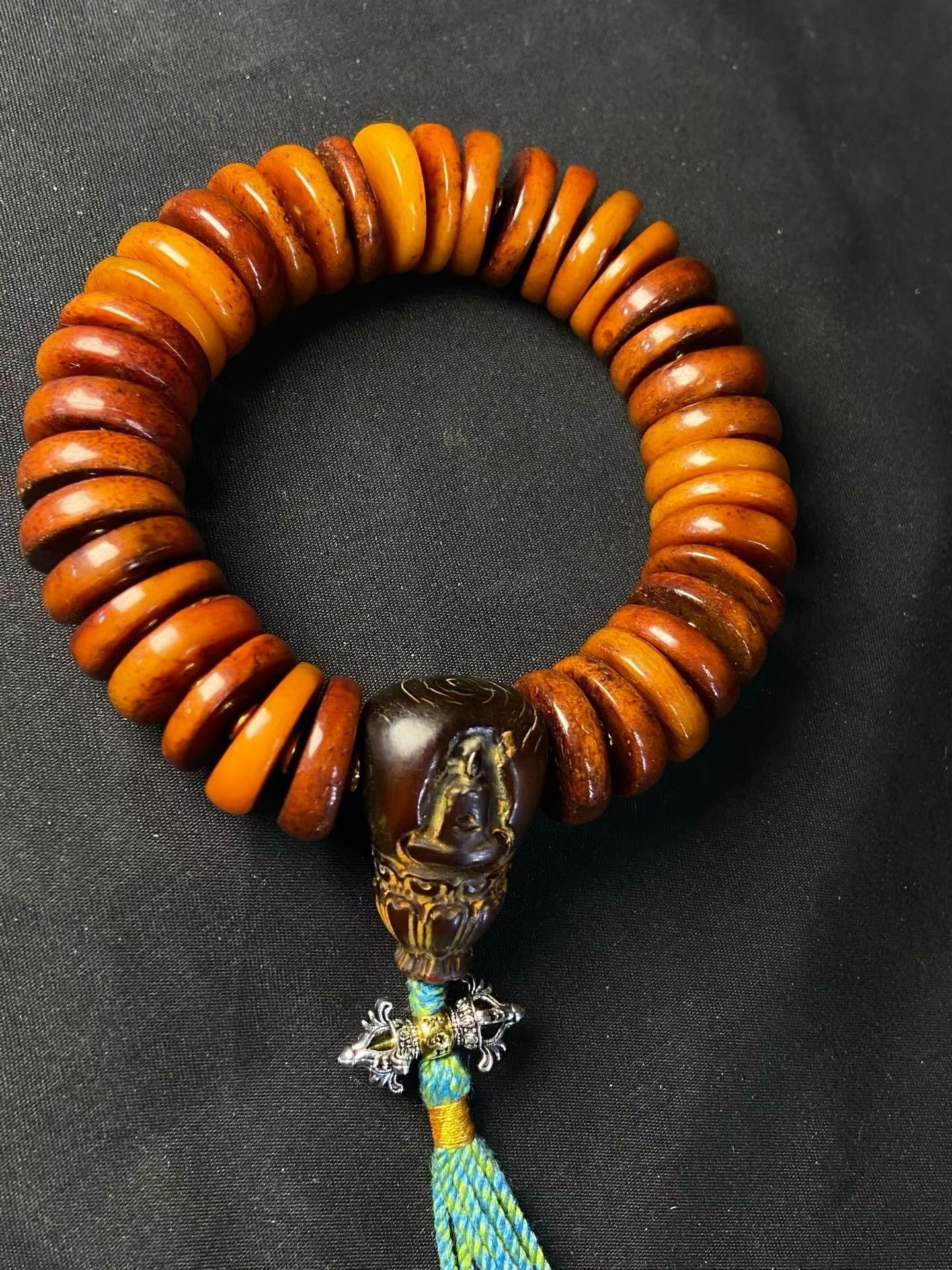 Stacked amber disc beads with a carved buddha head and a silvered vajra pendant