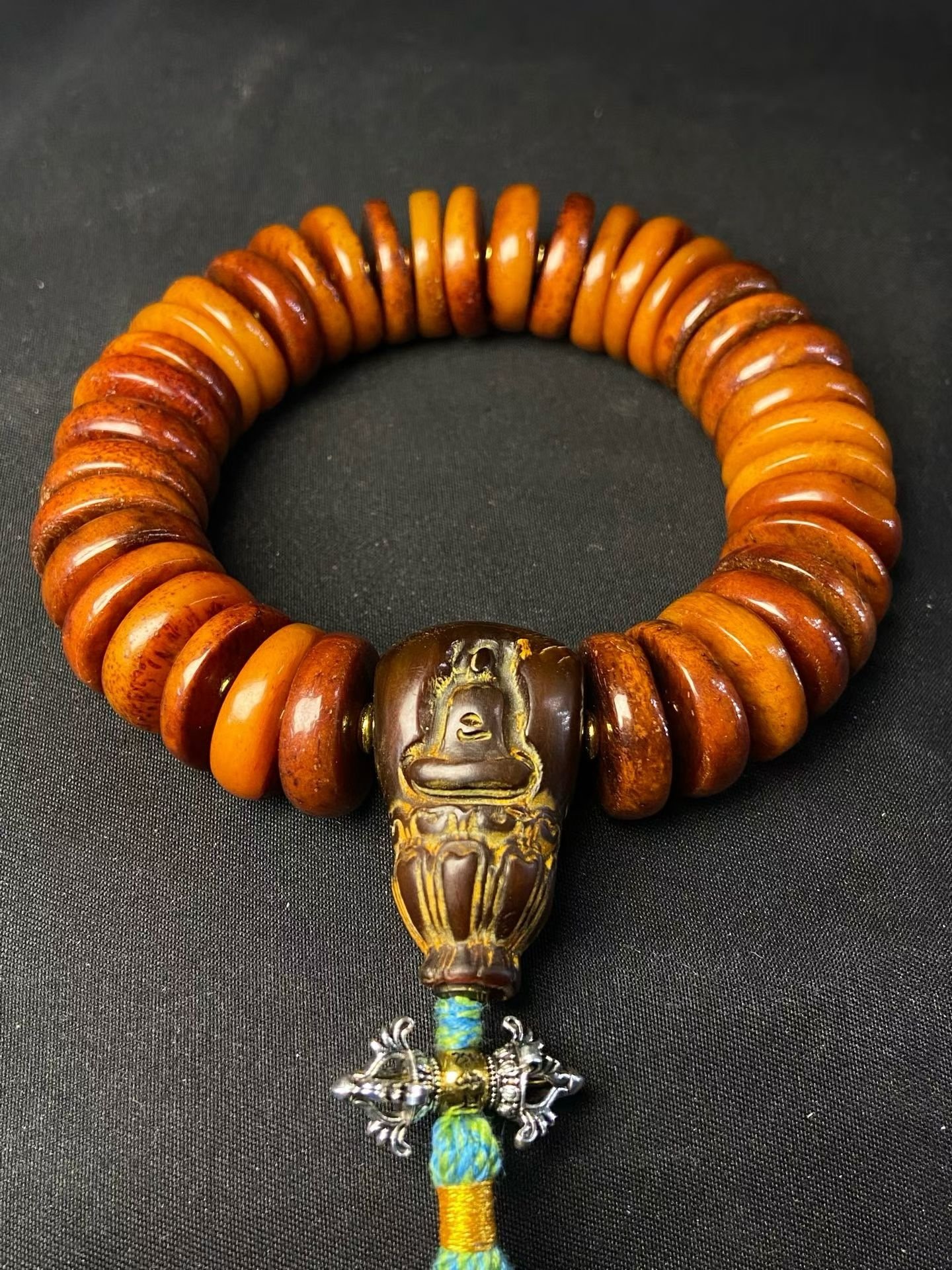 Stacked amber disc beads with a carved buddha head and a silvered vajra pendant