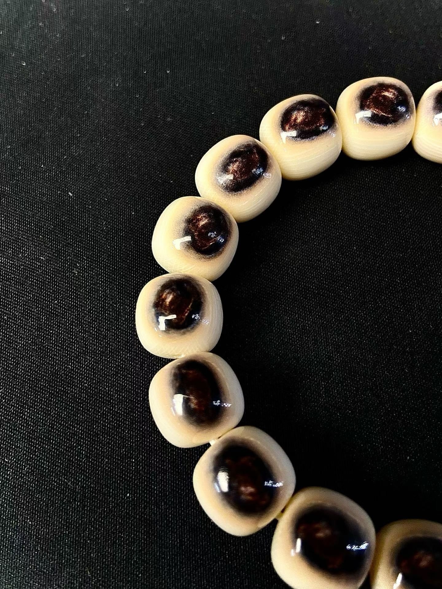 Cream barrel-shaped beads each with a single dark eye-shaped marking