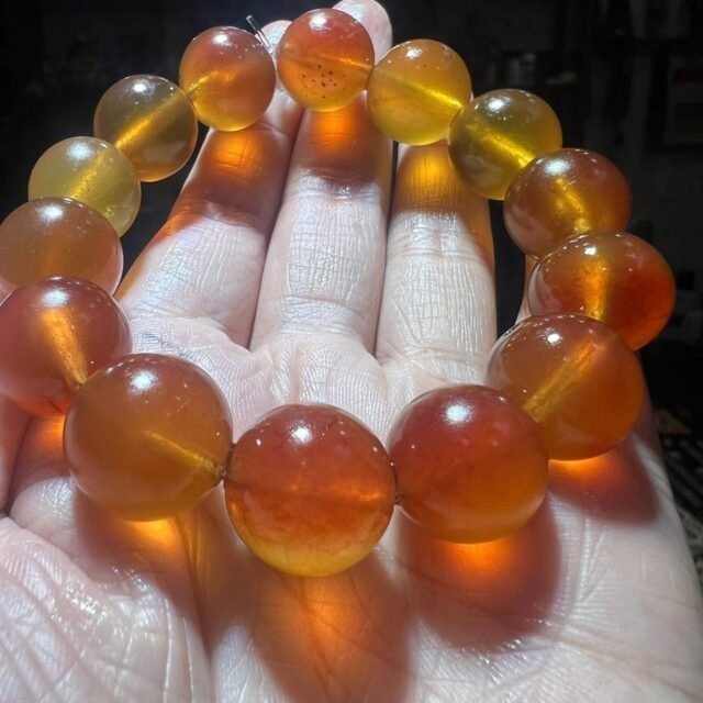 Translucent honey-coloured amber bracelet held in a hand with light passing through