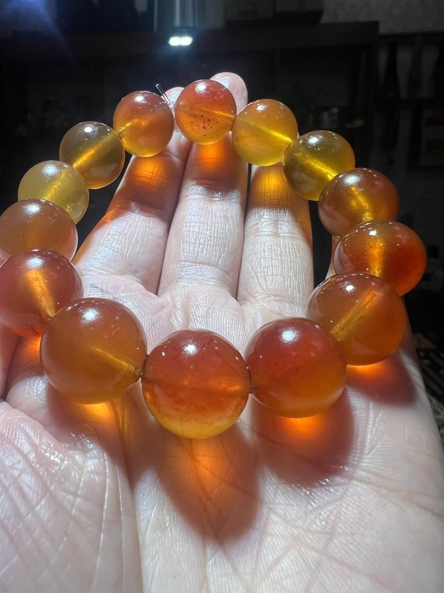 Translucent honey-coloured amber bracelet held in a hand with light passing through