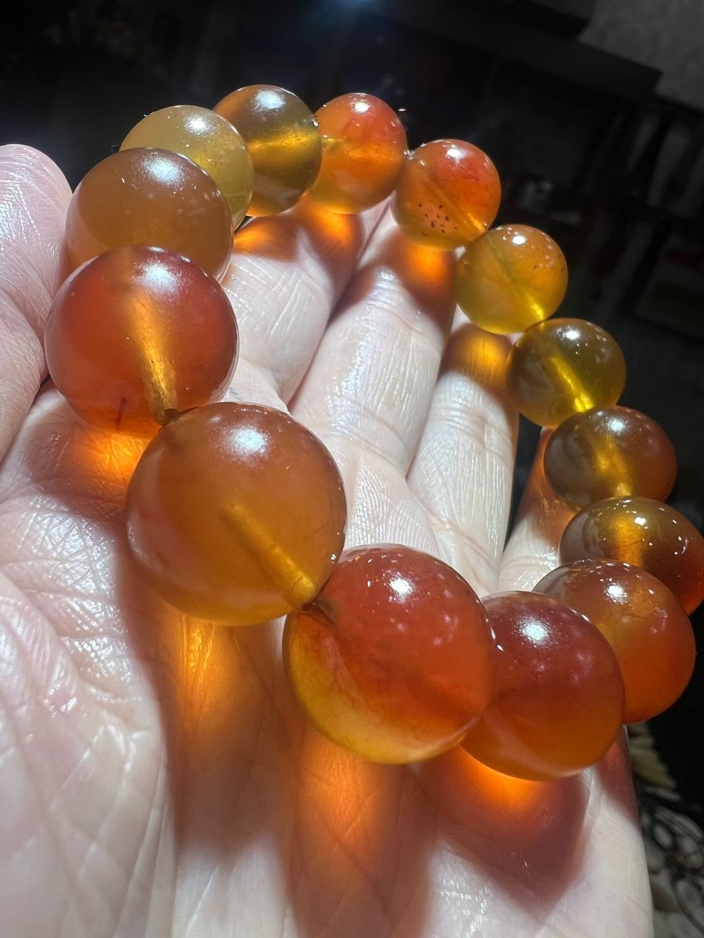 Translucent honey-coloured amber bracelet held in a hand with light passing through