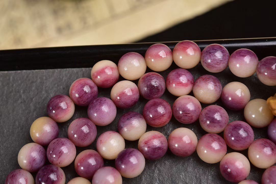 A 108-bead mala in mottled pink and purple stone on a dark stand