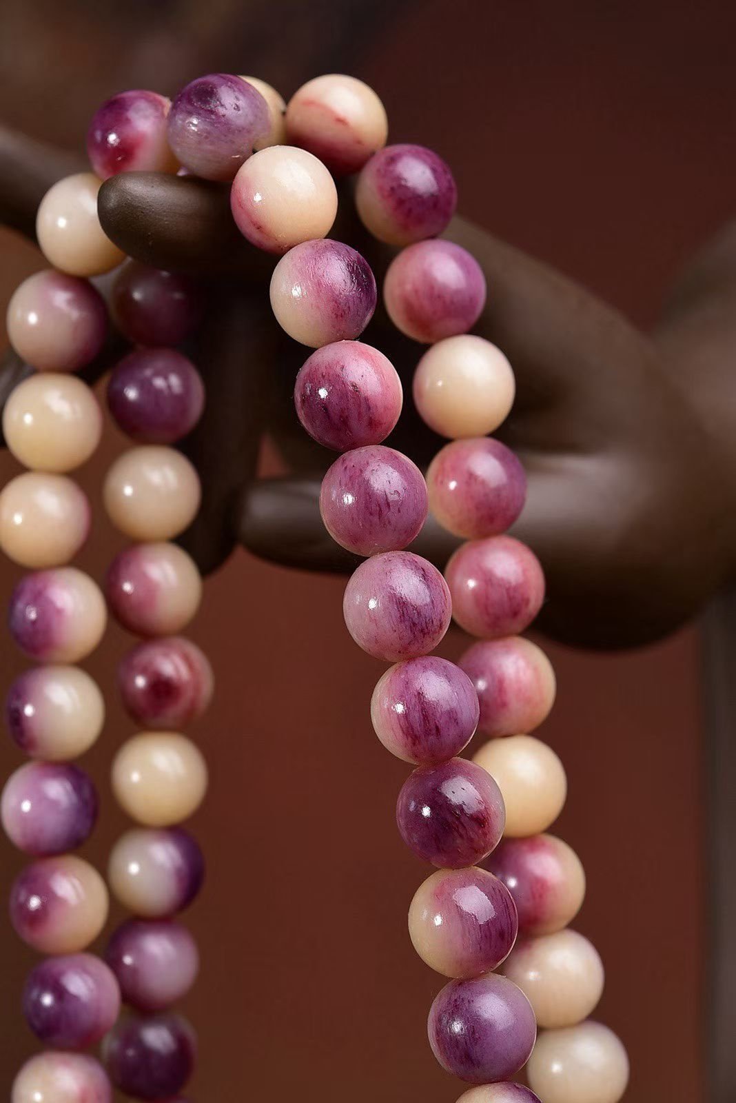 A 108-bead mala in mottled pink and purple stone on a dark stand