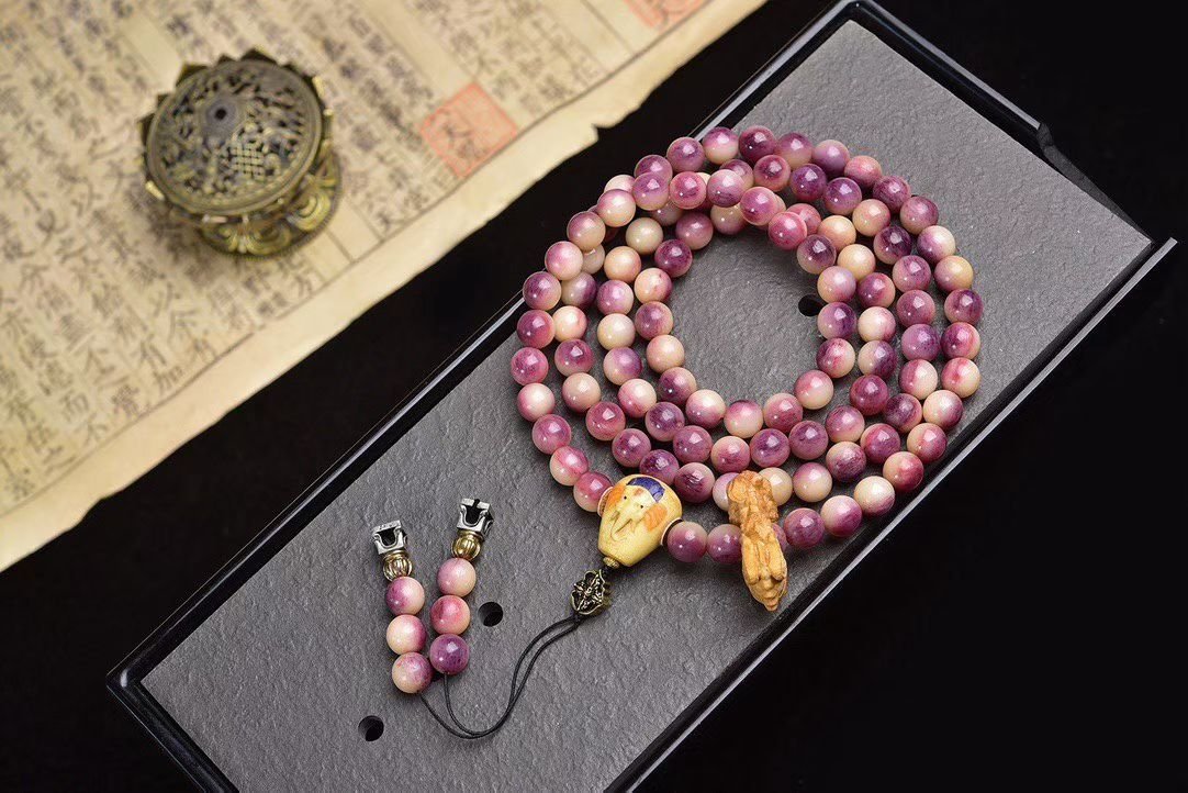 A 108-bead mala in mottled pink and purple stone on a dark stand