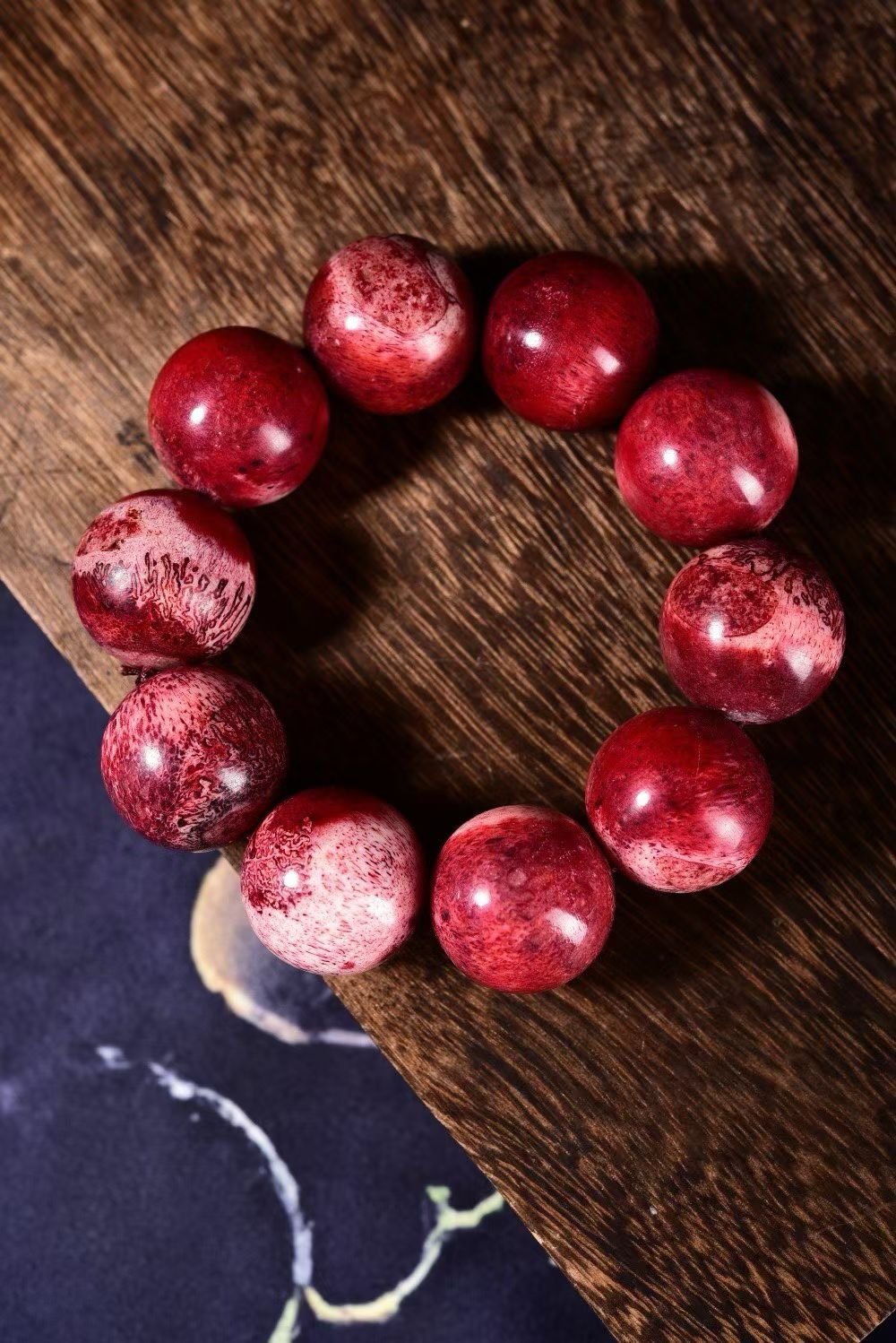 Deep red bracelet with white cloud-like veining, on dark wood